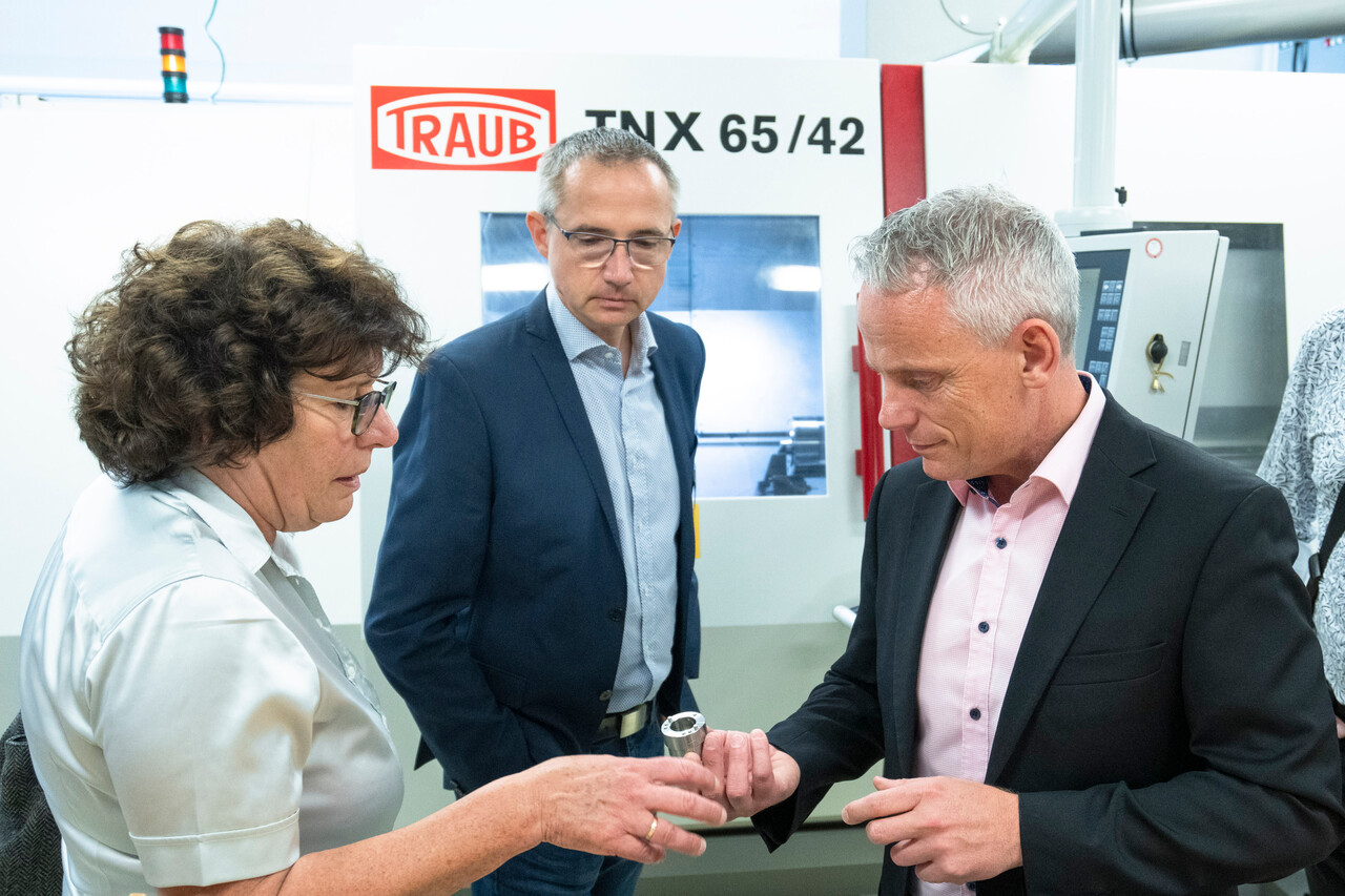 District Mayor Maren Schellenberg (Green party) and State Secretary Tino Schopf (SPD) look at a CNC-machined component that Department Manager Thomas Müller (mi.) shows them.
