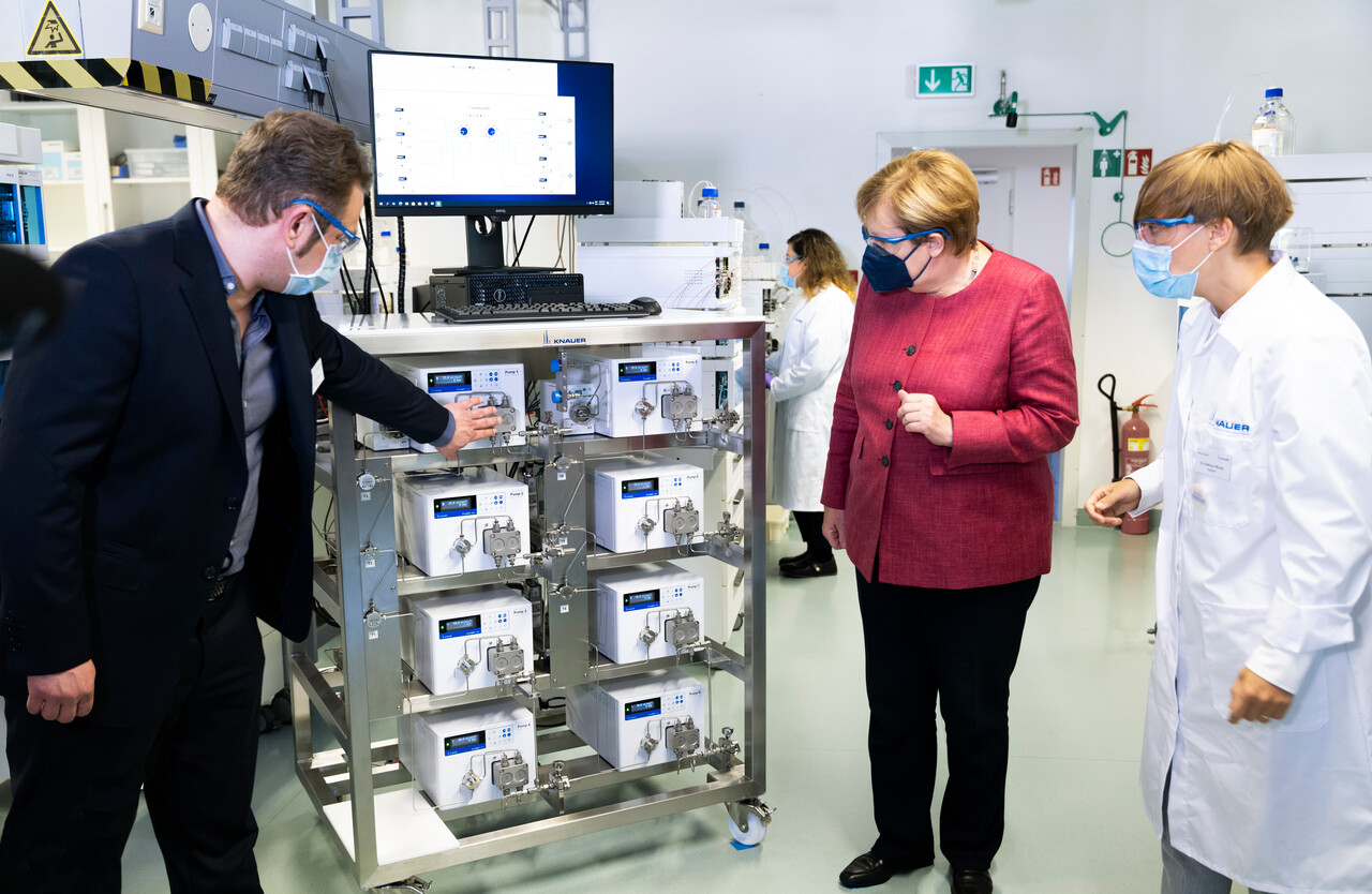 Geschäftsführer und Leiterin des Zentrallabors erklären der Bundeskanzlerin ein IJM-Skid zur Lipid-Nanopartikel-Herstellung